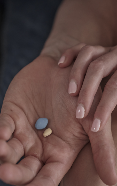 A man is holding ED pills in his hand, while his partner touches his hand